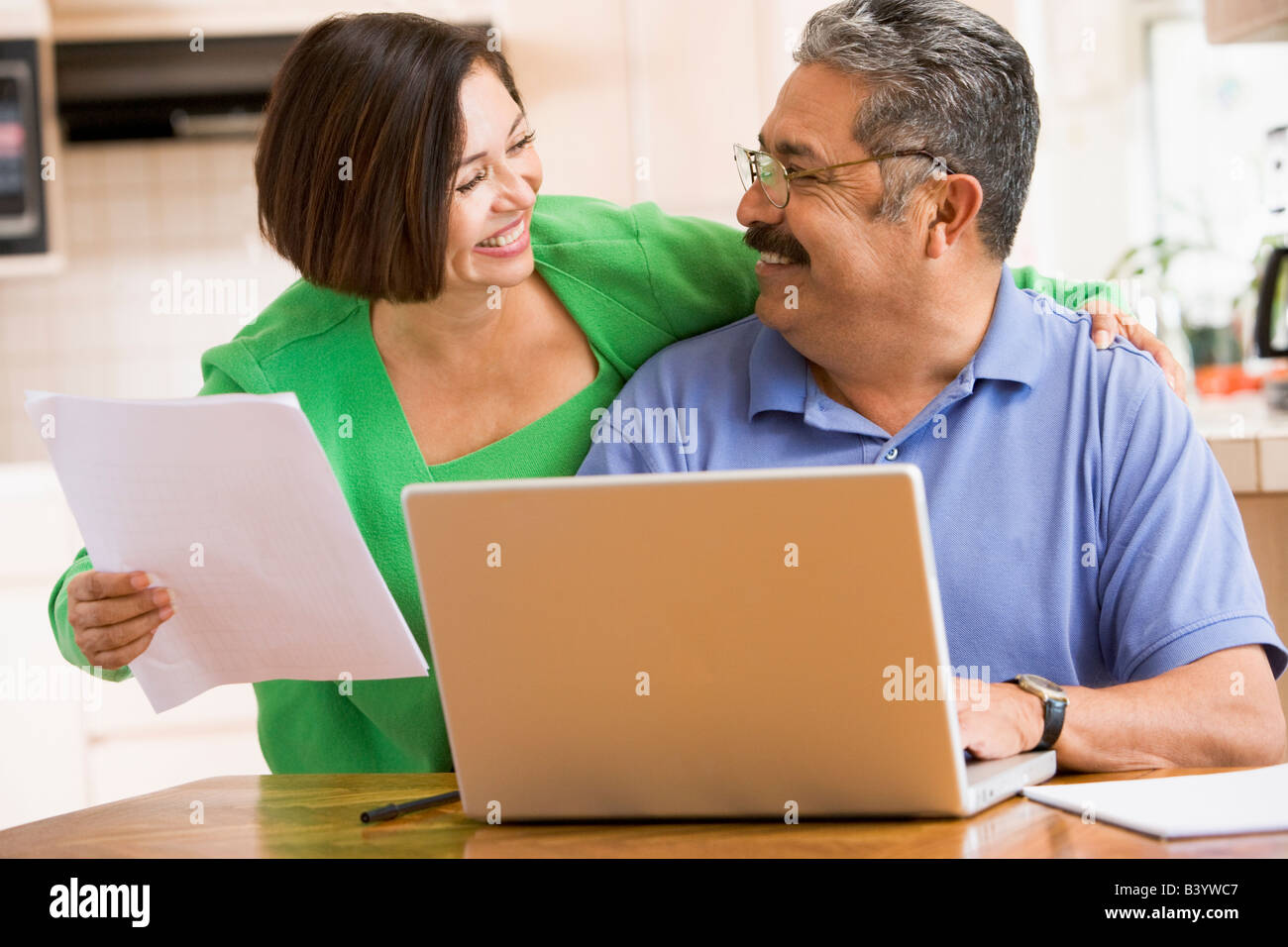 Couple in kitchen with laptop and paperwork smiling Stock Photo - Alamy
