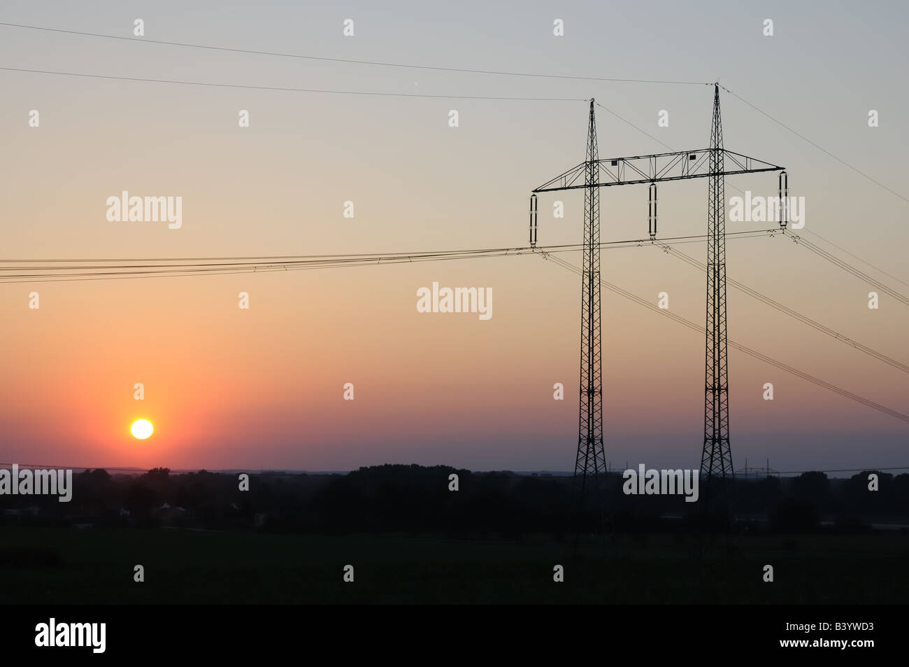 High voltage electricity pylons on a field at sunset. Stock Photo
