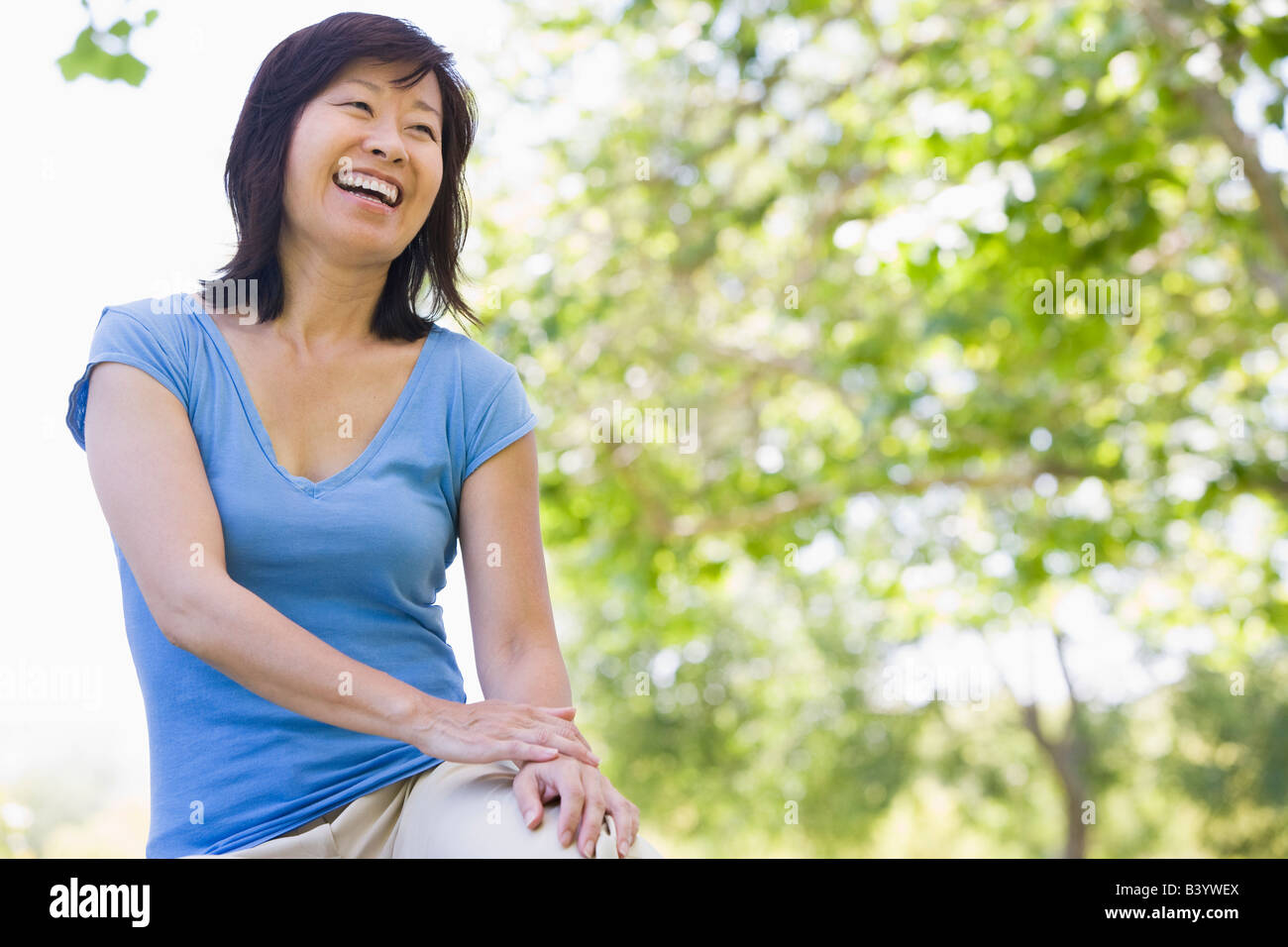 Woman sitting outdoors smiling Stock Photo - Alamy