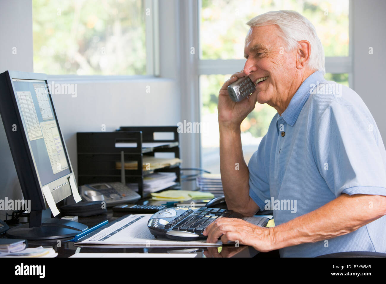 Man in home office on telephone using computer smiling Stock Photo