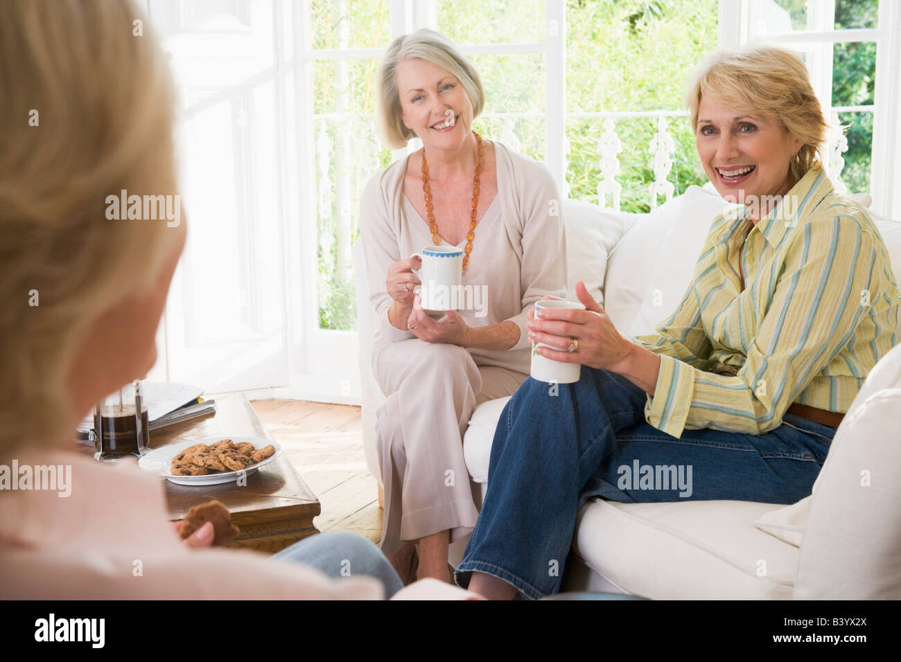 Three women in living room with coffee smiling Stock Photo - Alamy