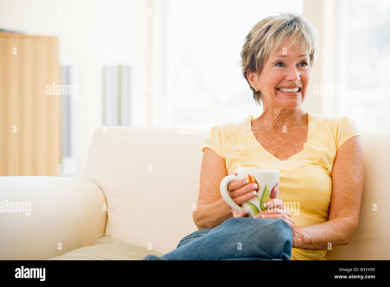 Woman relaxing in living room with coffee smiling Stock Photo - Alamy