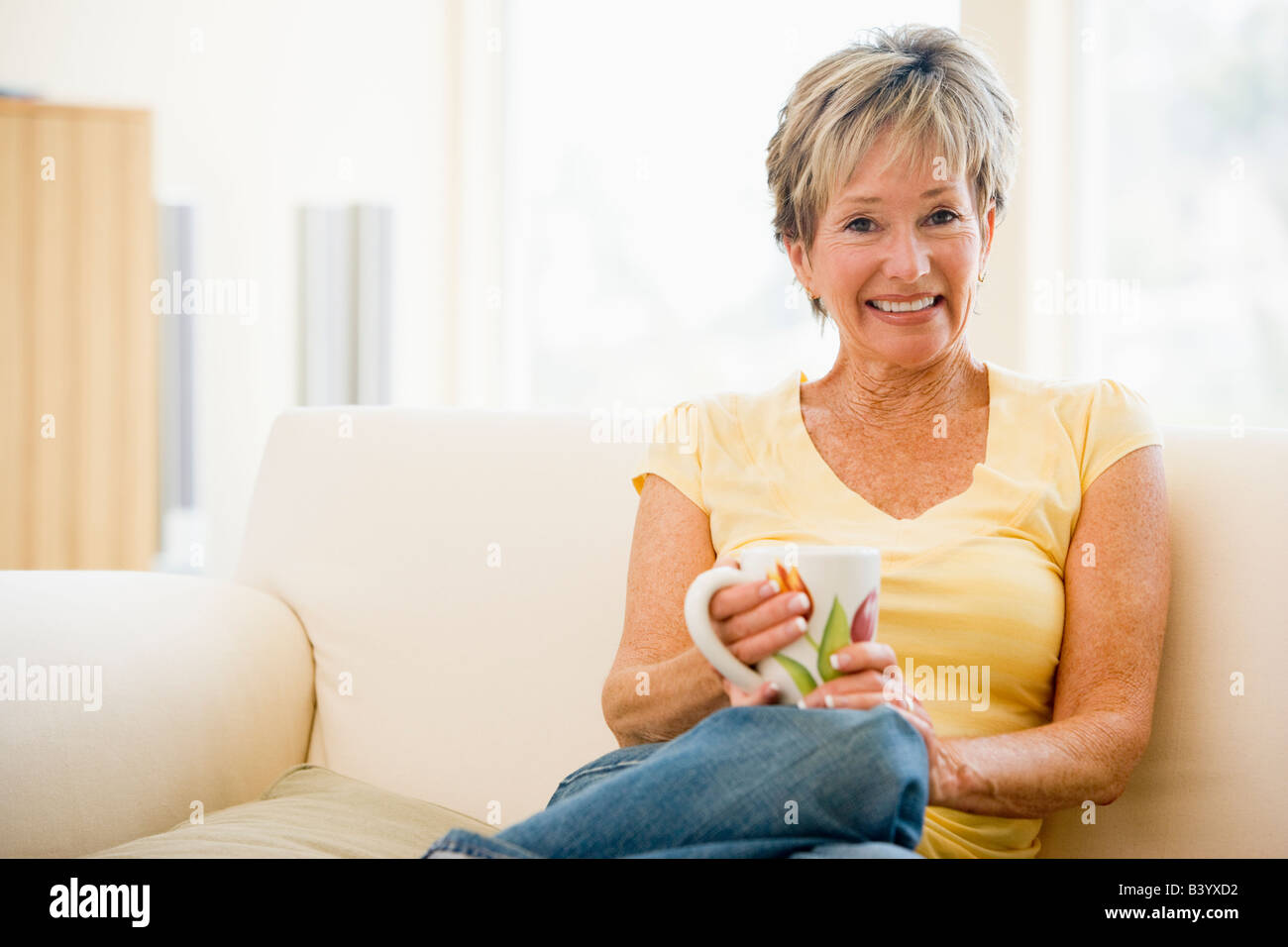 Woman sitting in living room with coffee smiling Stock Photo - Alamy