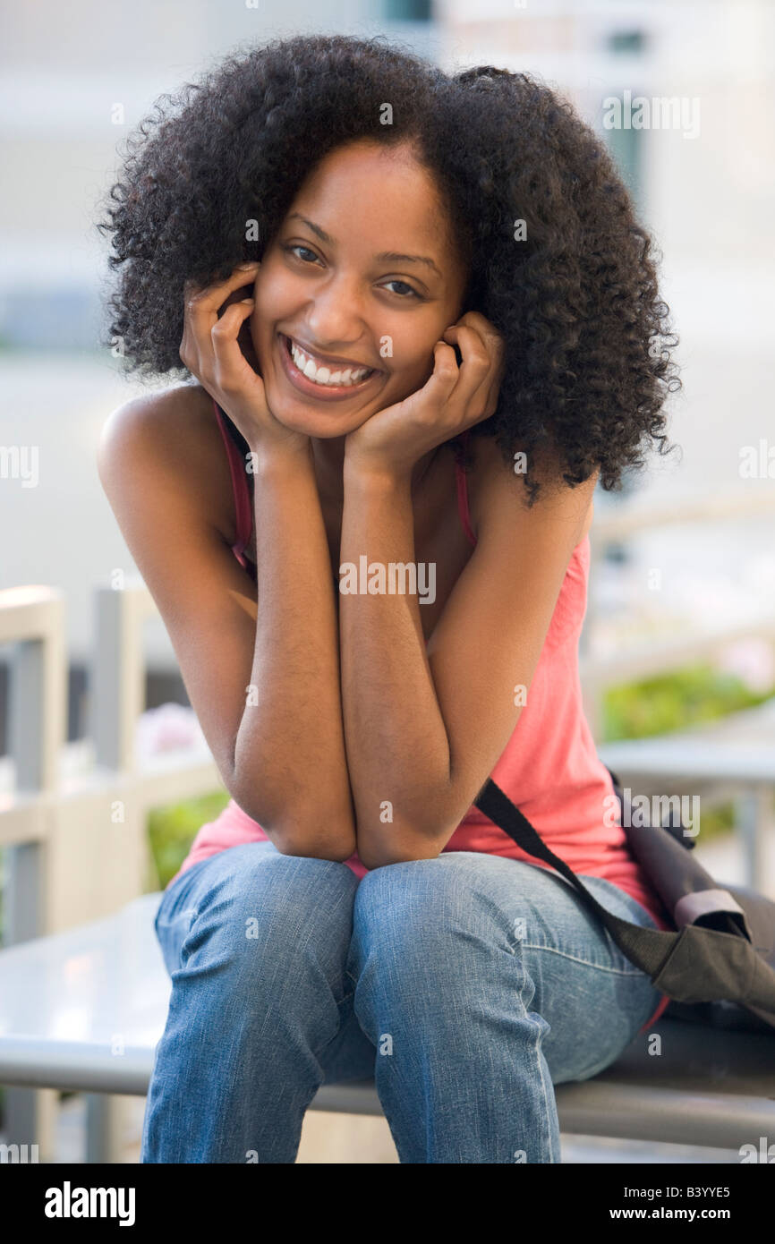 Woman sitting on bench outdoors smiling (selective focus) Stock Photo