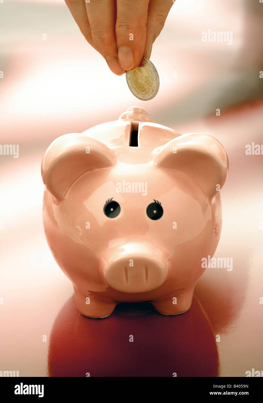 Hand putting a coin into a piggy bank Stock Photo - Alamy
