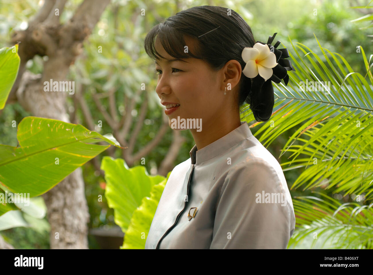 Female Staff member of The Oriental Hotel Bangkok. tropical gardens Frangipani flower in her hair smiling welcoming Travel Asia Stock Photo