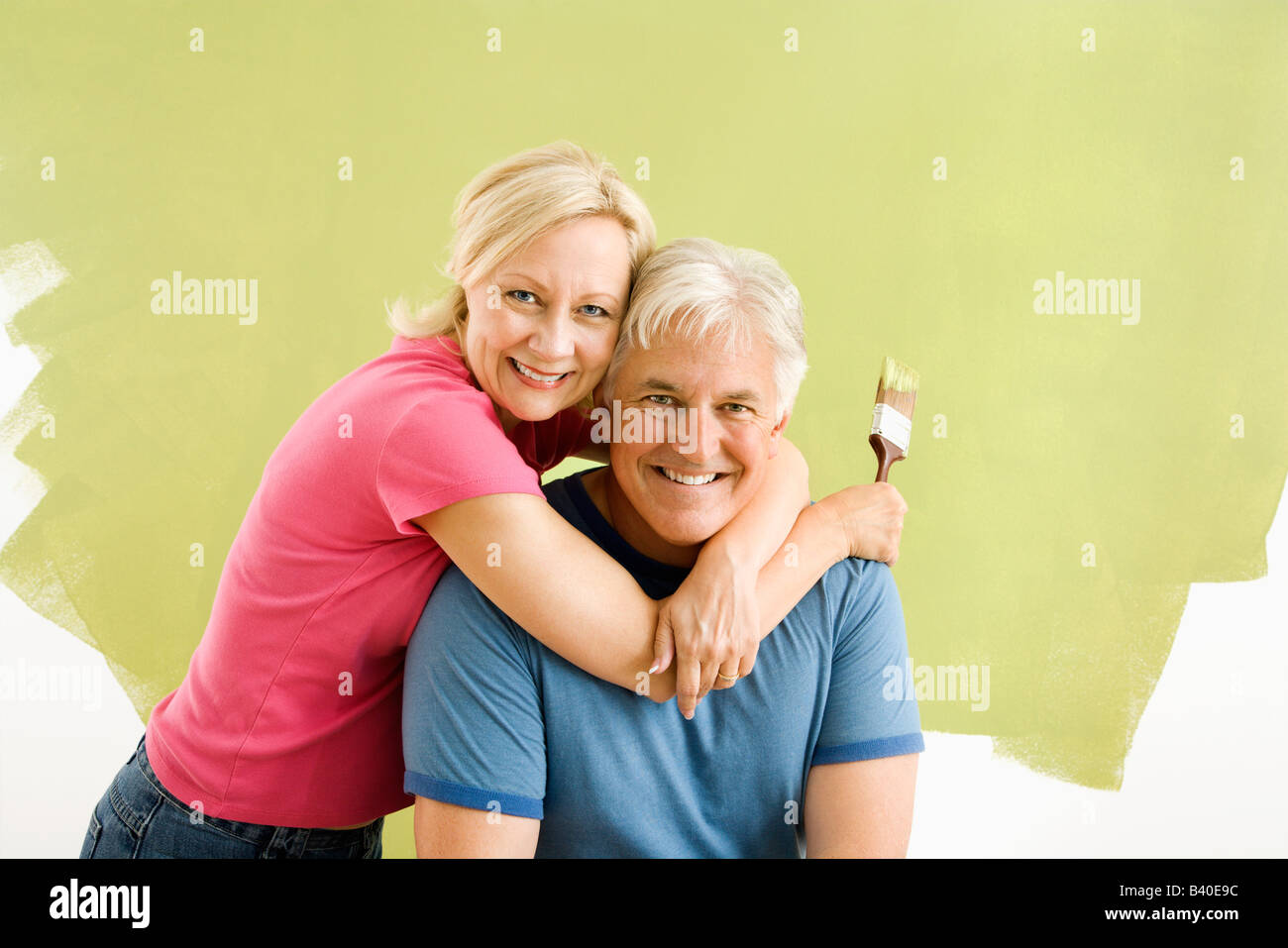 Portrait of smiling adult couple sitting in front of half painted wall with paintbrushes Stock Photo