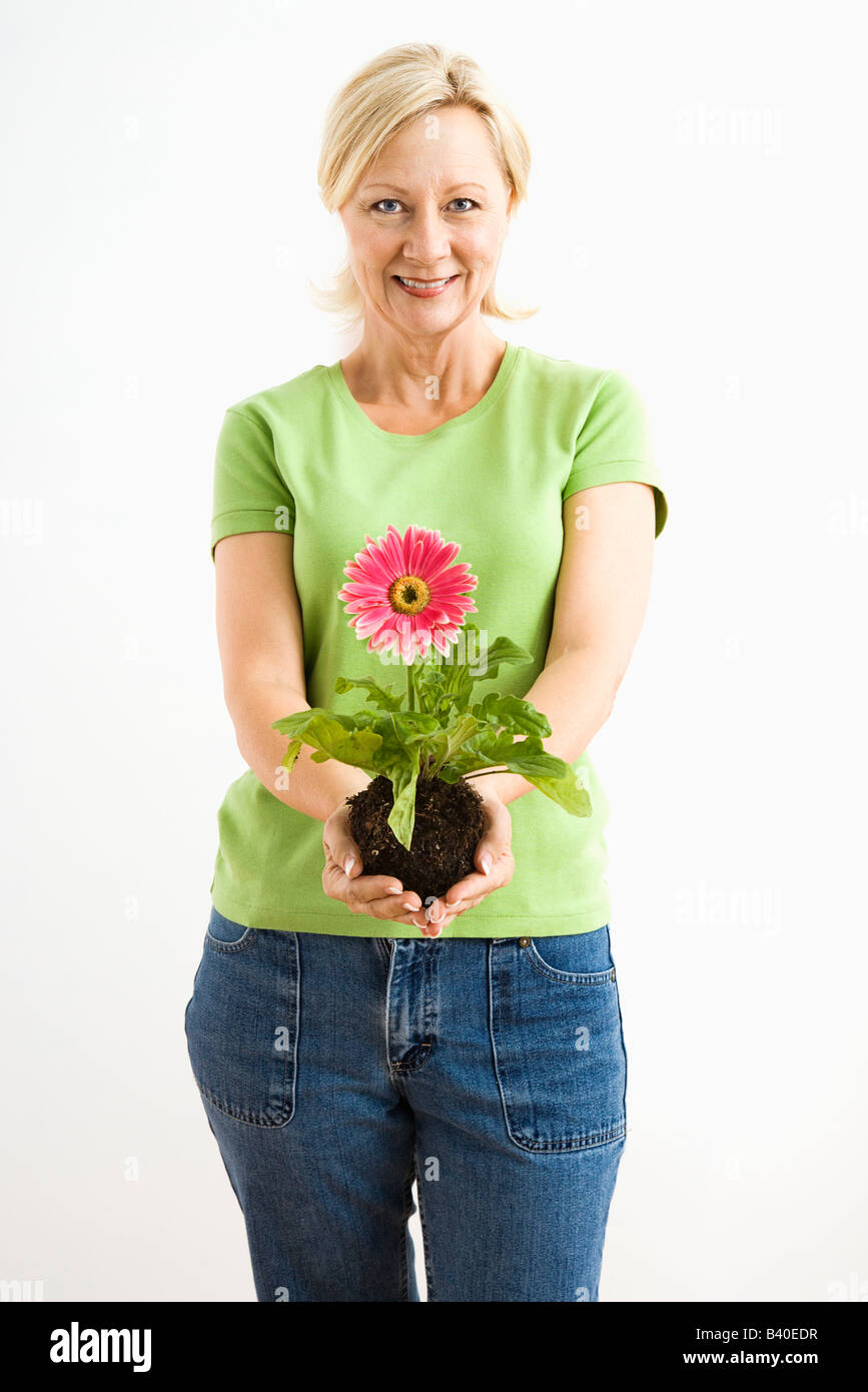 Portrait of smiling adult blonde woman standing holding pink gerber daisy plant Stock Photo
