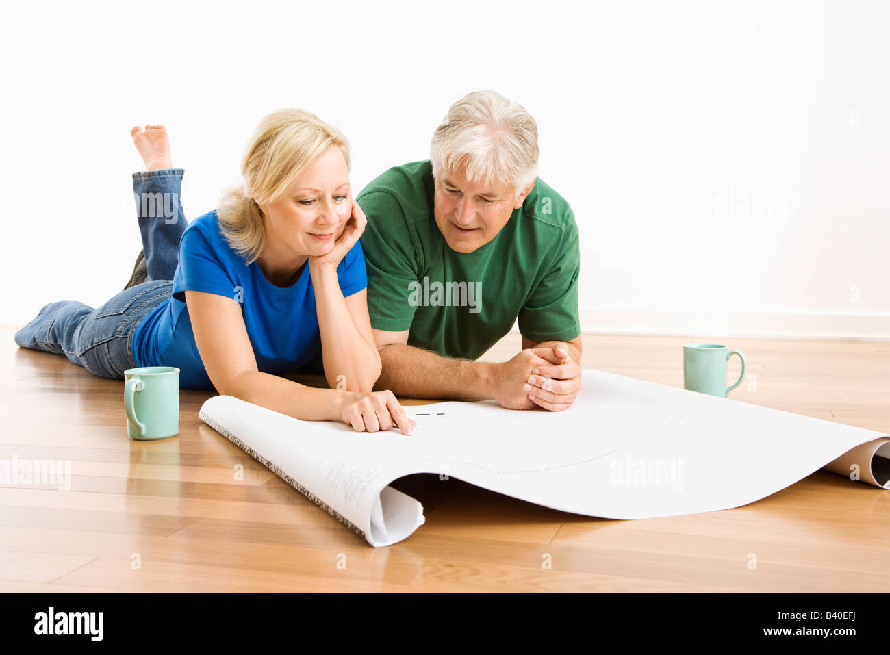 Middle aged couple lying on floor looking at architectural blueprints together Stock Photo