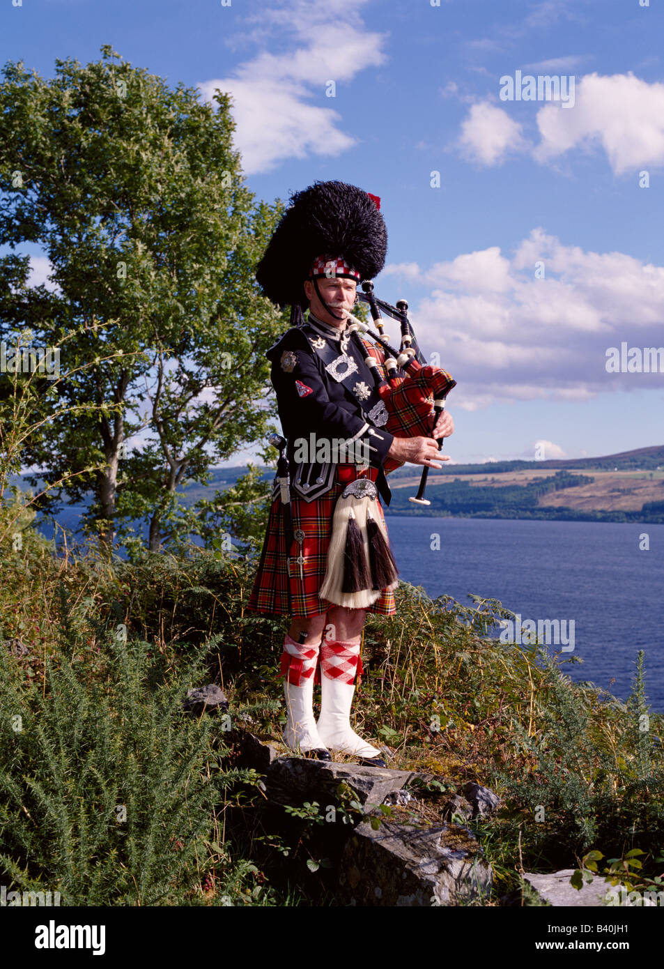 dh  SCOTTISH PIPER SCOTLAND Bagpipes tartan kilt bagpipe in highlands bag pipes player bagpiper traditional highland dress male loch ness Stock Photo