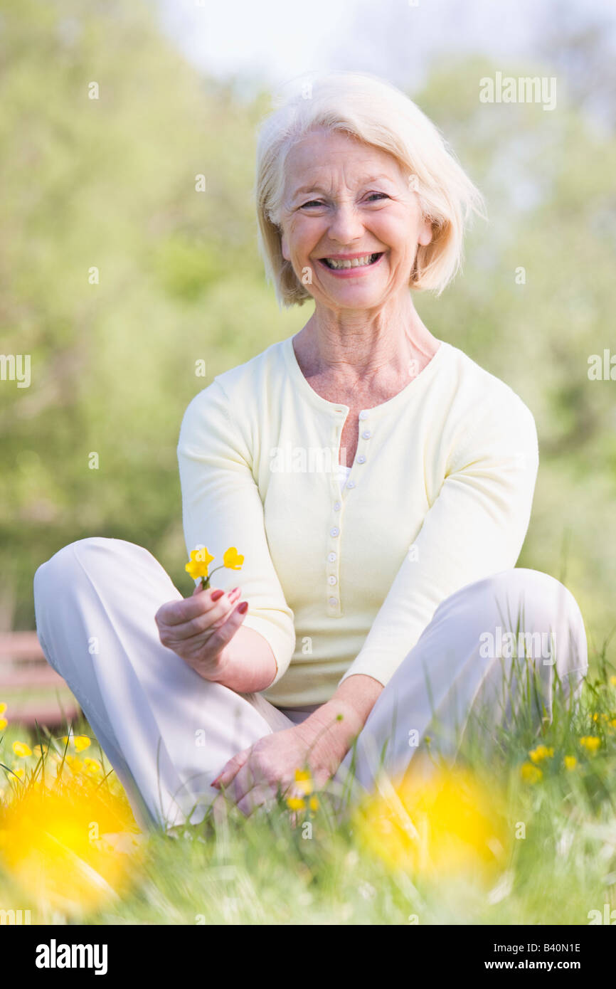 Woman sitting outdoors smiling and holding a Buttercup flower Stock Photo