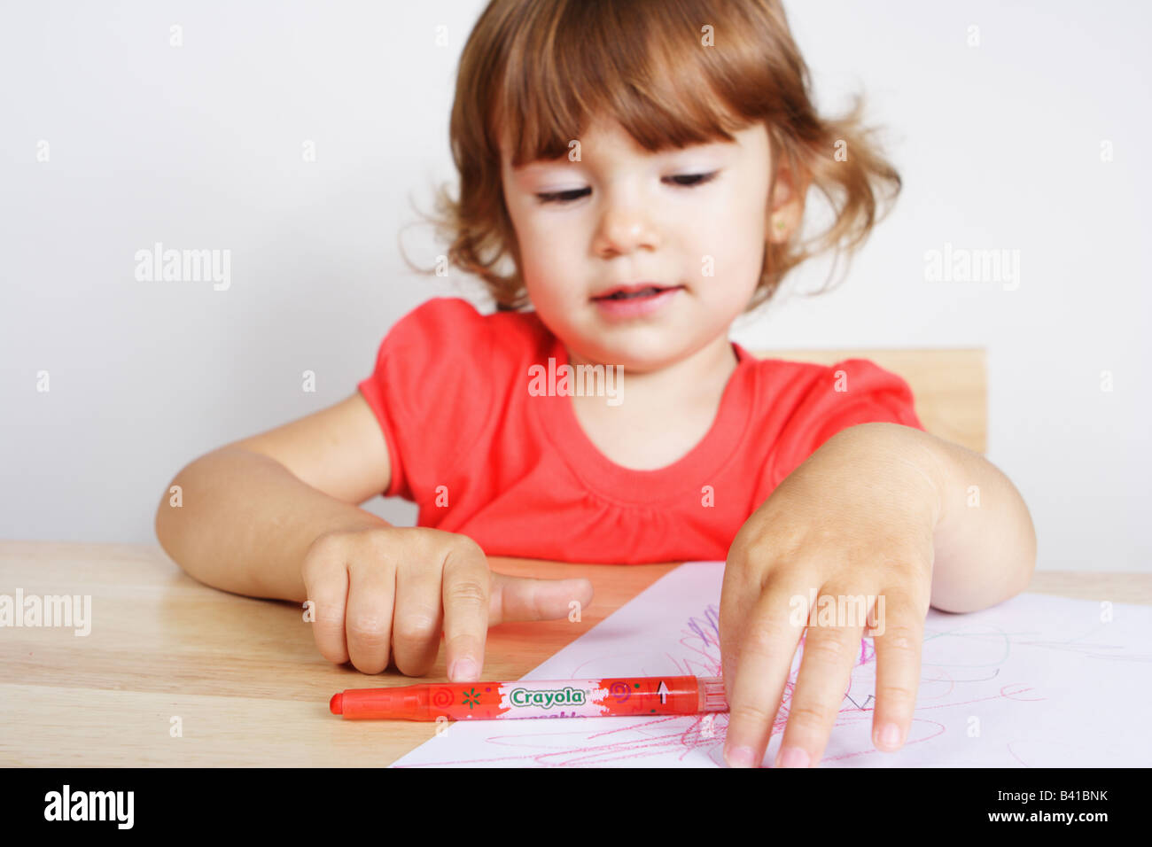 A two years old toddler girl at her drawing desk is playing with a red