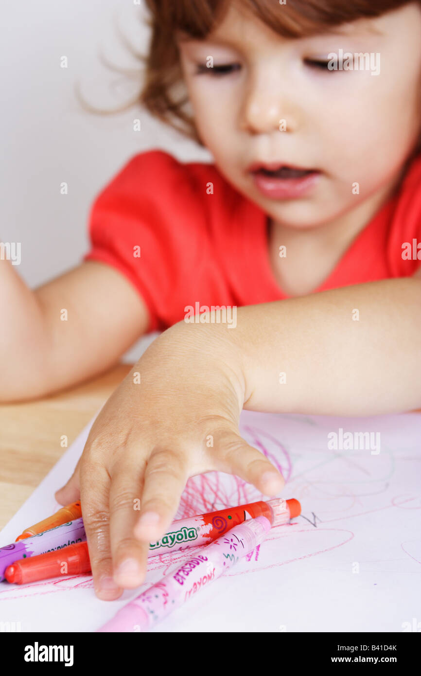 A two years old toddler girl is picking up a colored crayon at her