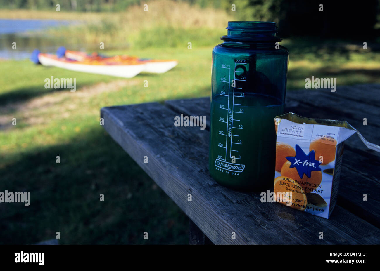 Orange juice concentrate and water bottle on wooden table in front of two kayaks near Flen, Sweden, August 2006 Stock Photo