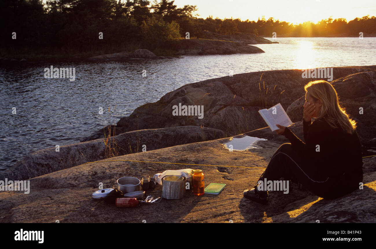 Younger woman reading a book at sunset on island of baltic sea archipelago Sodermanlands Lan Sweden August 2006 Stock Photo
