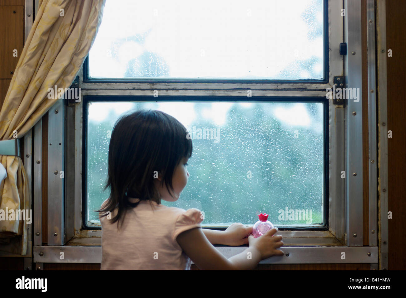 A four year old girl playing in the window of a moving train. Stock Photo