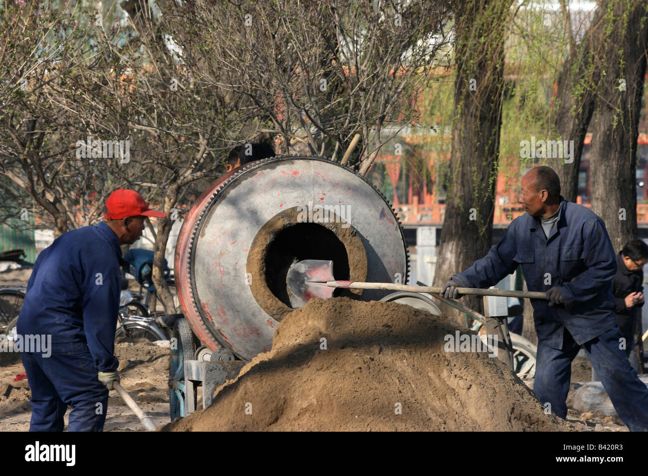 Two workers shovelling sand into a concrete mixer, Beijing, China Stock Photo