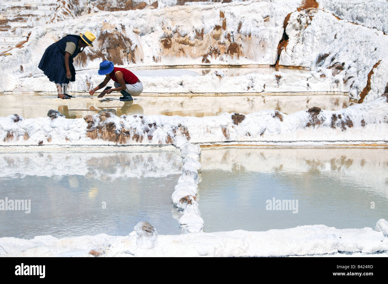 Two Indian women work extracting salt in the salt pools of Salineras de Mara near Cuzco, Peru. Stock Photo