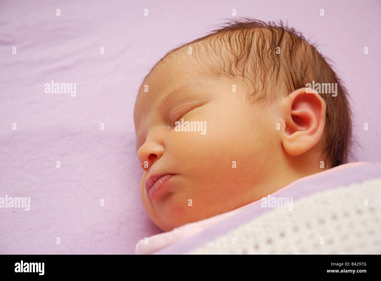 A one week old baby asleep under blankets Stock Photo