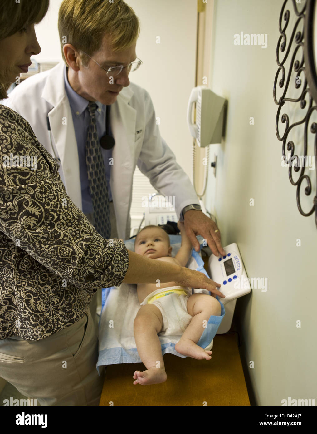A baby is weighed during a routine physical examination as his young grandmother looks on Stock