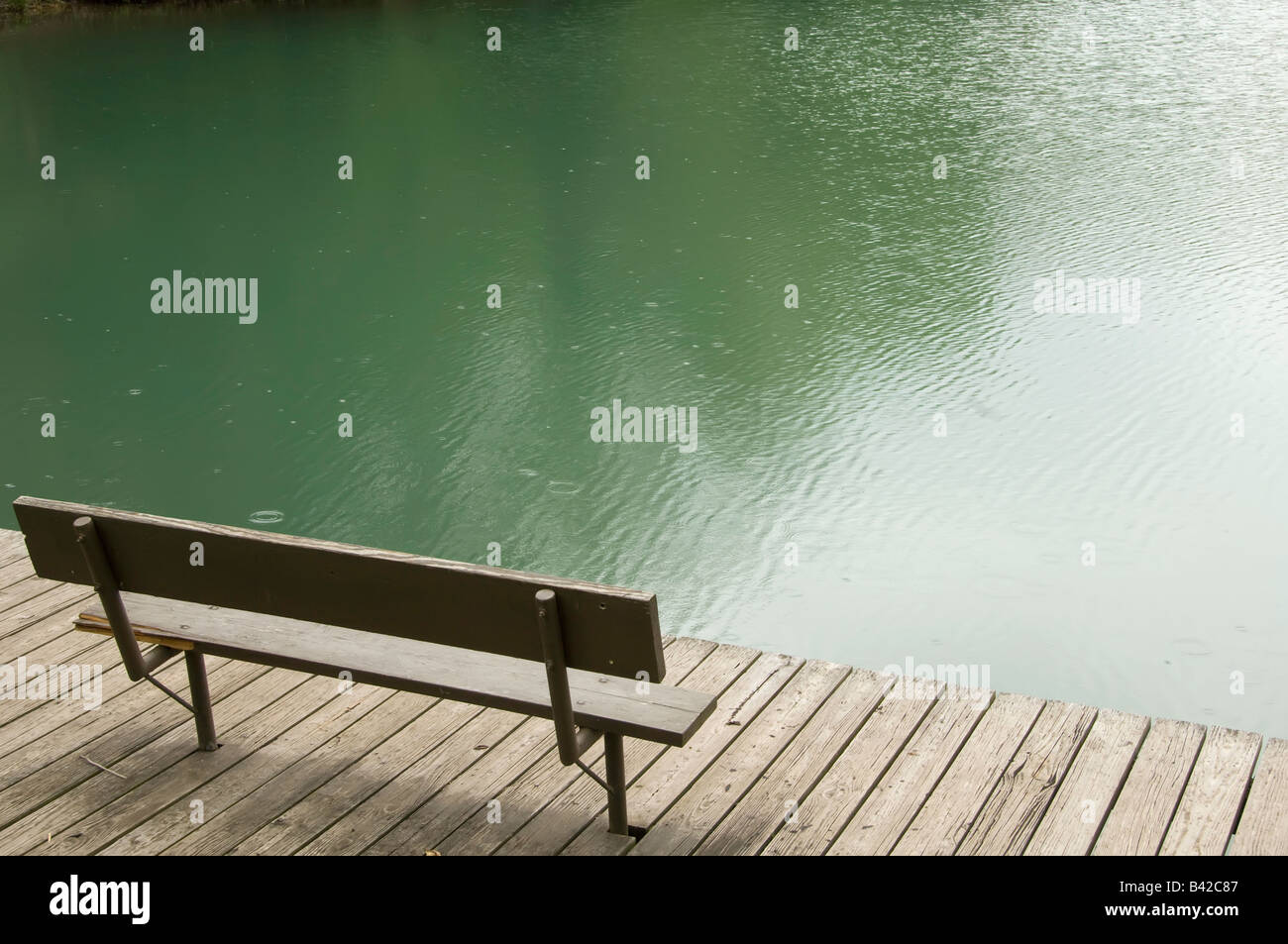 Vacant park bench on dock by lake in spring drizzle Stock Photo