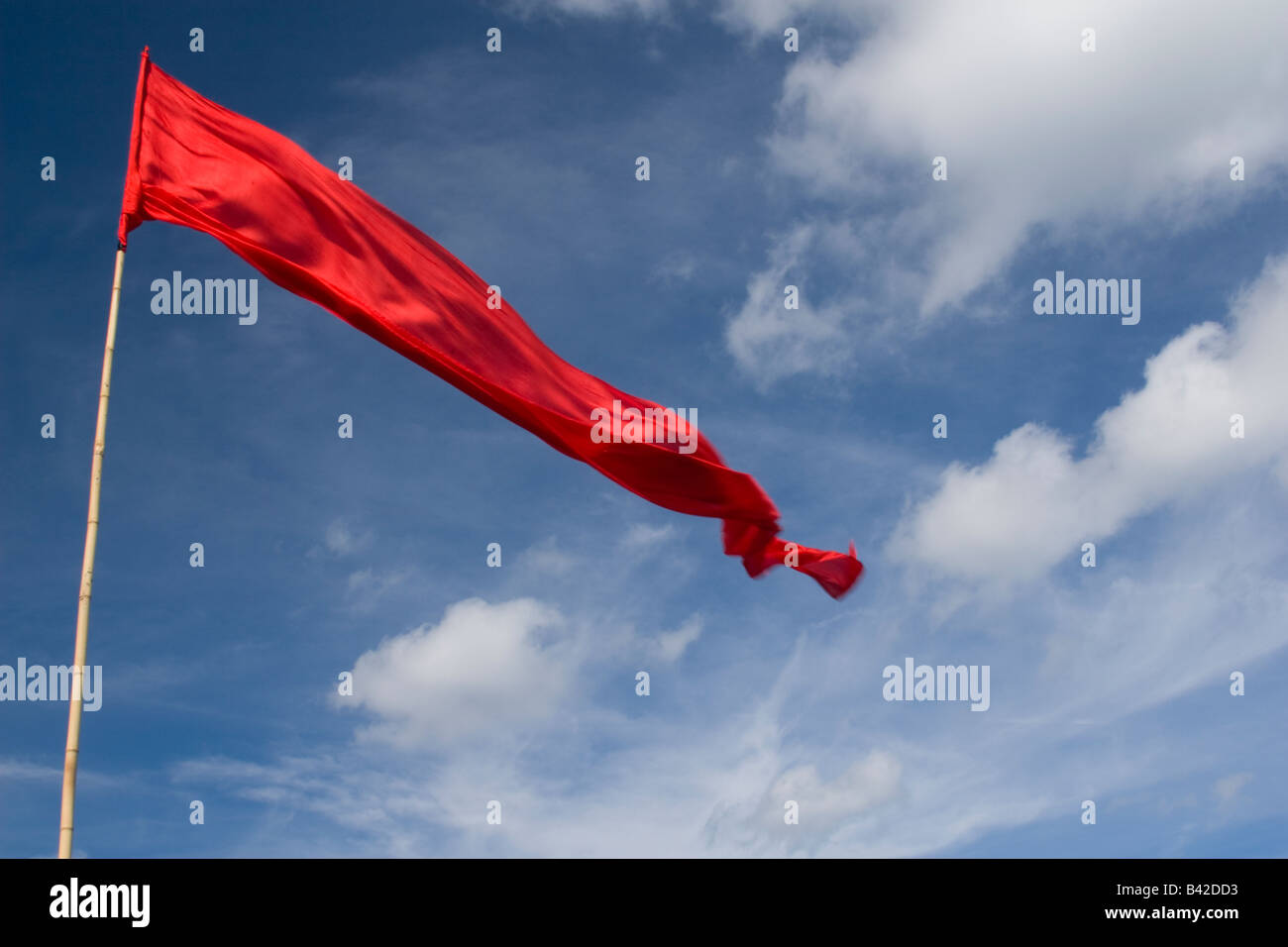 A very long red flag against a blue sky with white puffy clouds Stock