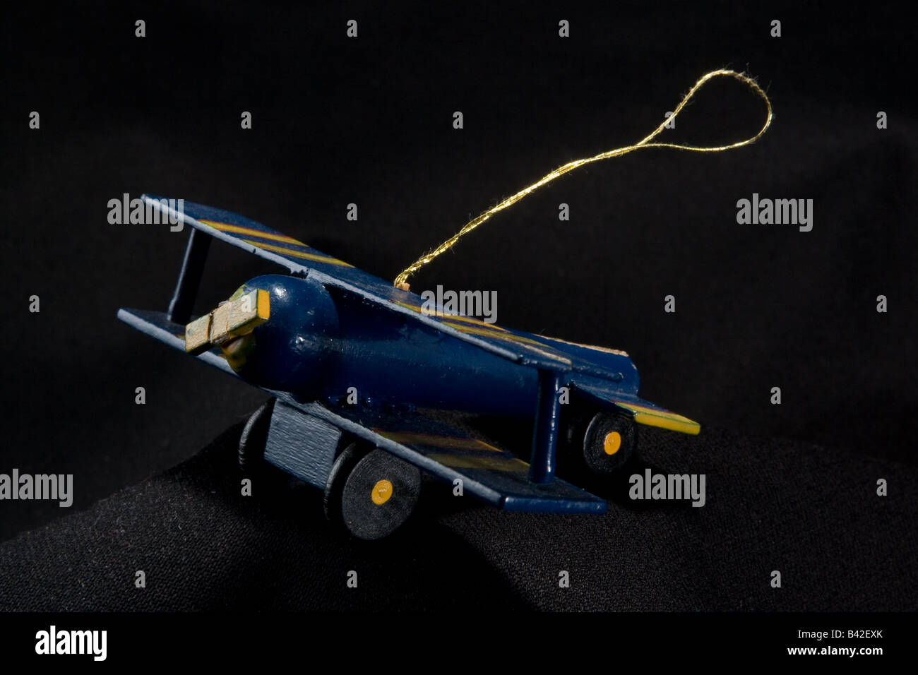 A blue and yellow wooden biplane used as a christmas ornament or decoration with a gold thread, against a black background. Stock Photo