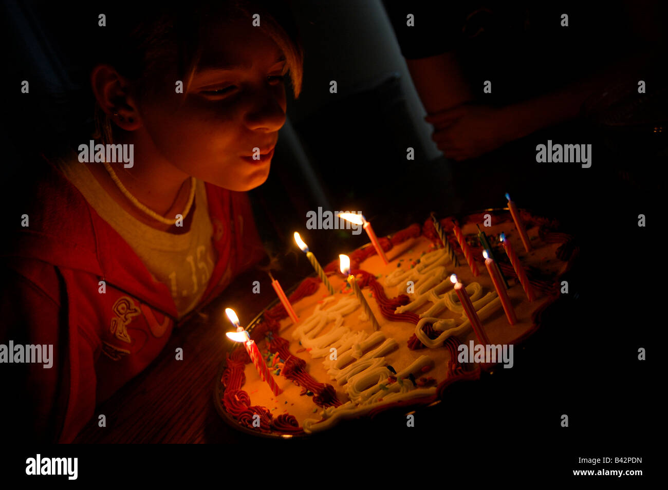 Pretty teen blond girl blowing out candles on a birthday cake in a low light environment. Stock Photo