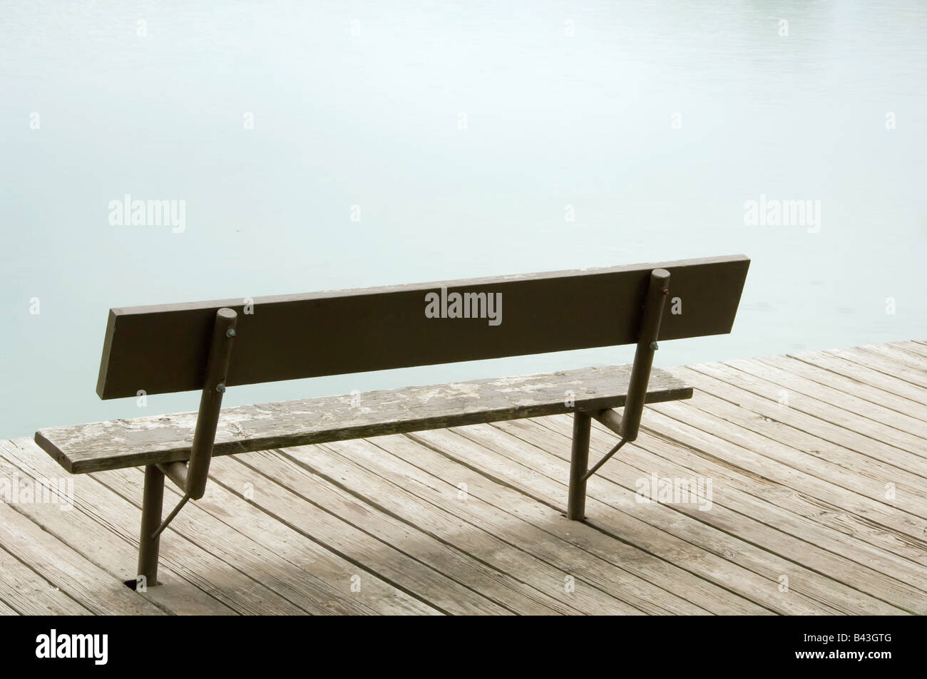 Weather beaten park bench on dock by lake Stock Photo