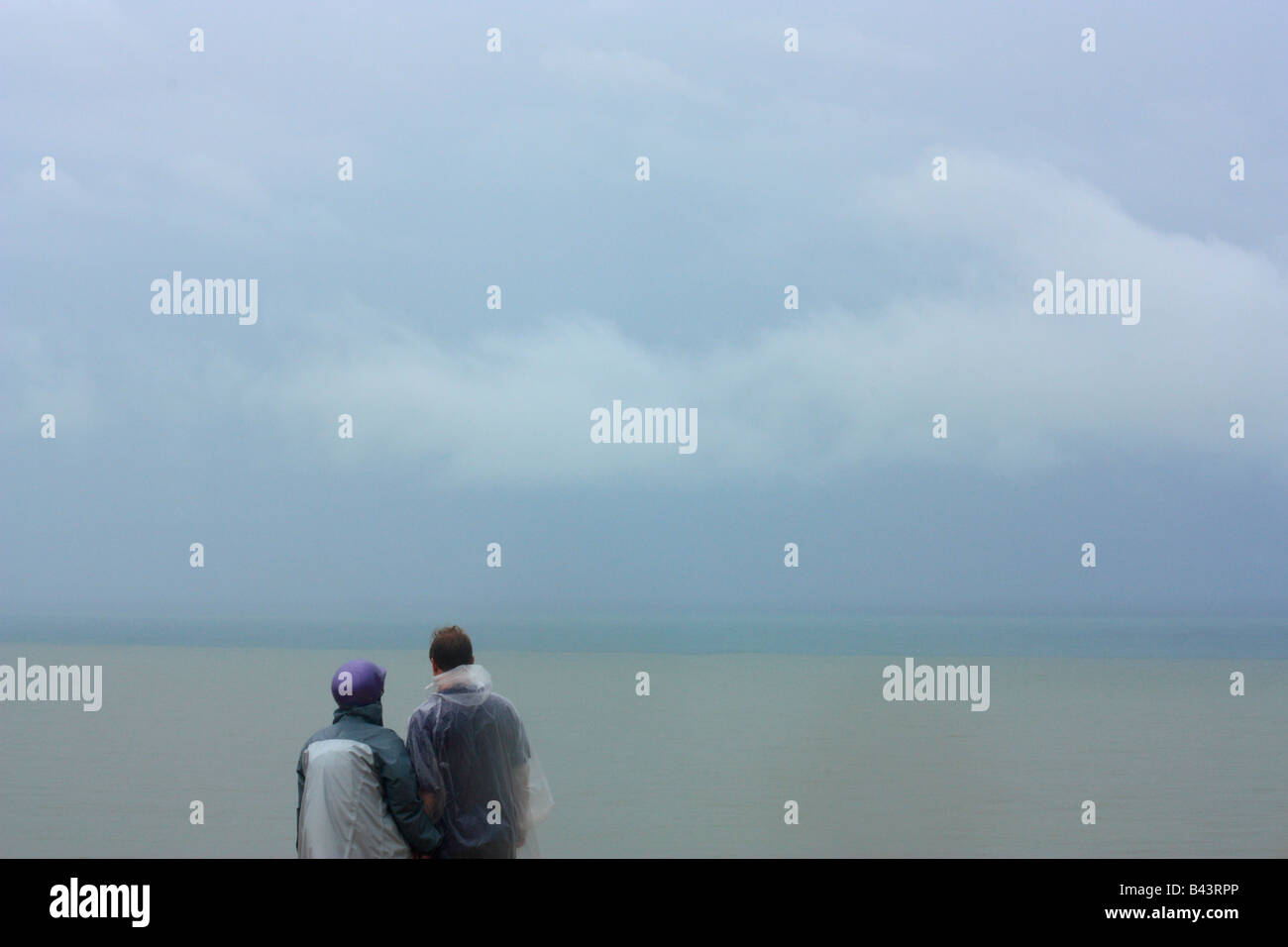 A couple looks out to sea in rainy weather. Stock Photo