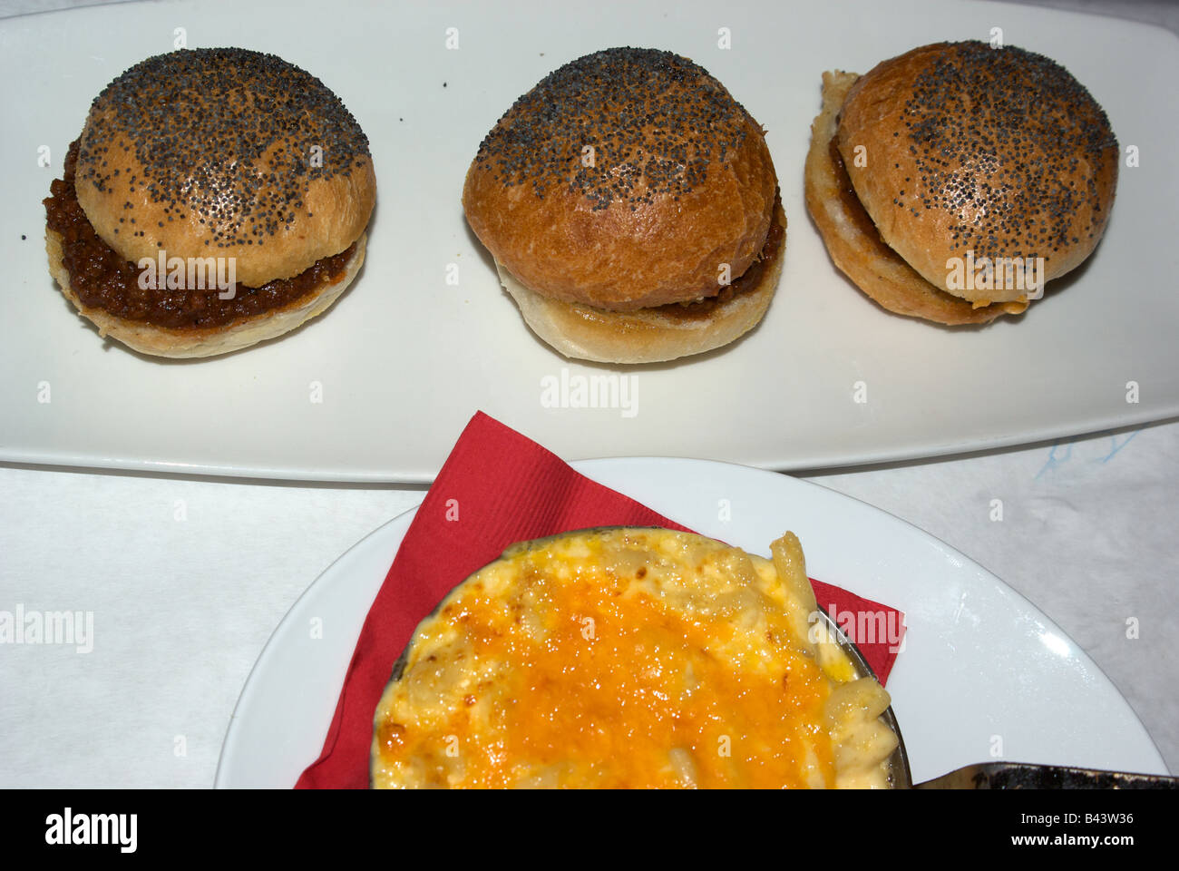 A trio of mini hamburger sliders in poppy seed buns with a side dish of baked macaroni and
