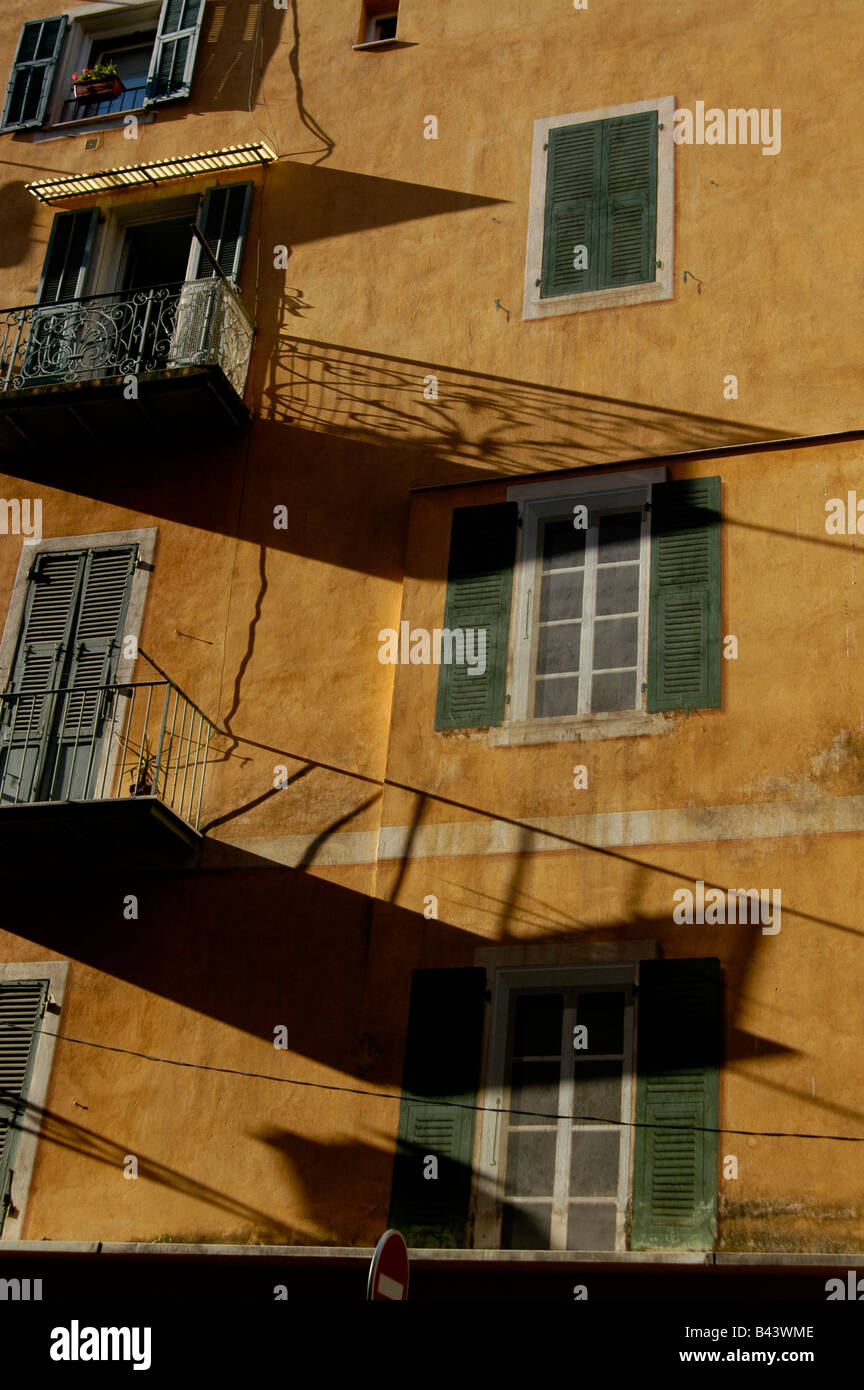 Balcony cast early morning shadows on painted images of shuttered windows on the side of a building in the Old town of Nice Stock Photo