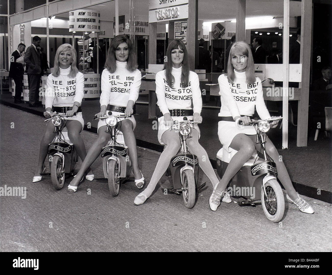 Business Efficiency Exhibition Four mini skirted messenger girls sit on Electric Scooters that they ride around exhibition Stock Photo