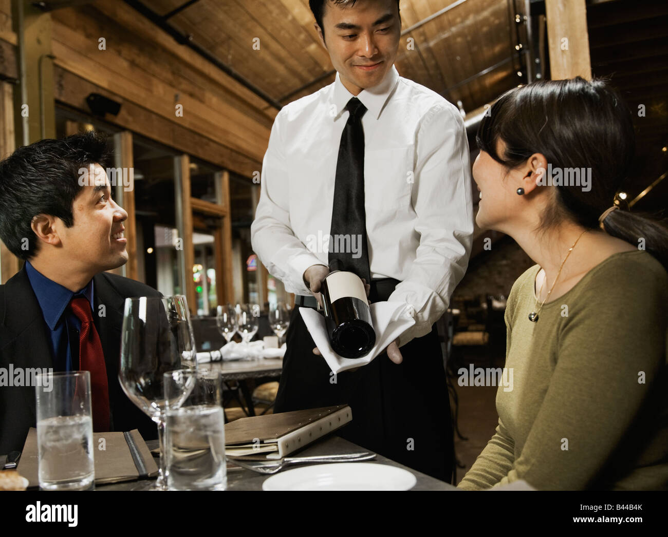 Asian waiter showing wine to couple Stock Photo