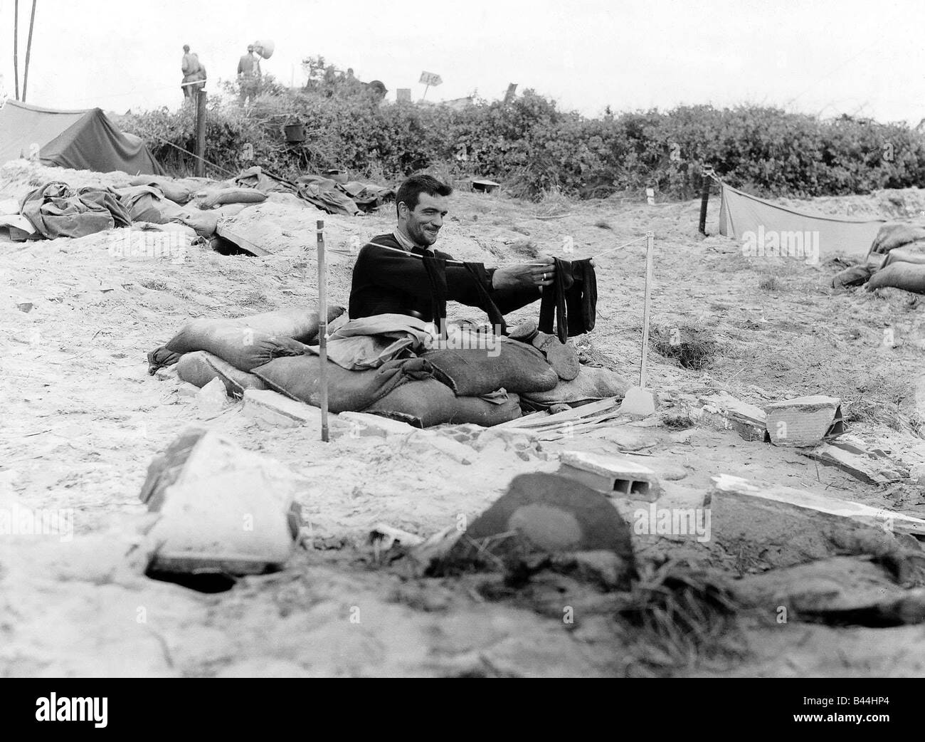A soldier hangs a pair of socks on a washing line outside his fox hole on a French beach during WW2 1944 1940s Stock Photo