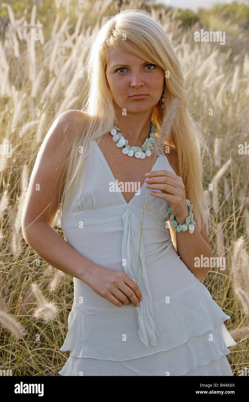 Outdoor Portrait of a Young Blonde Girl in a White Dress in a Field of Grass Stock Photo