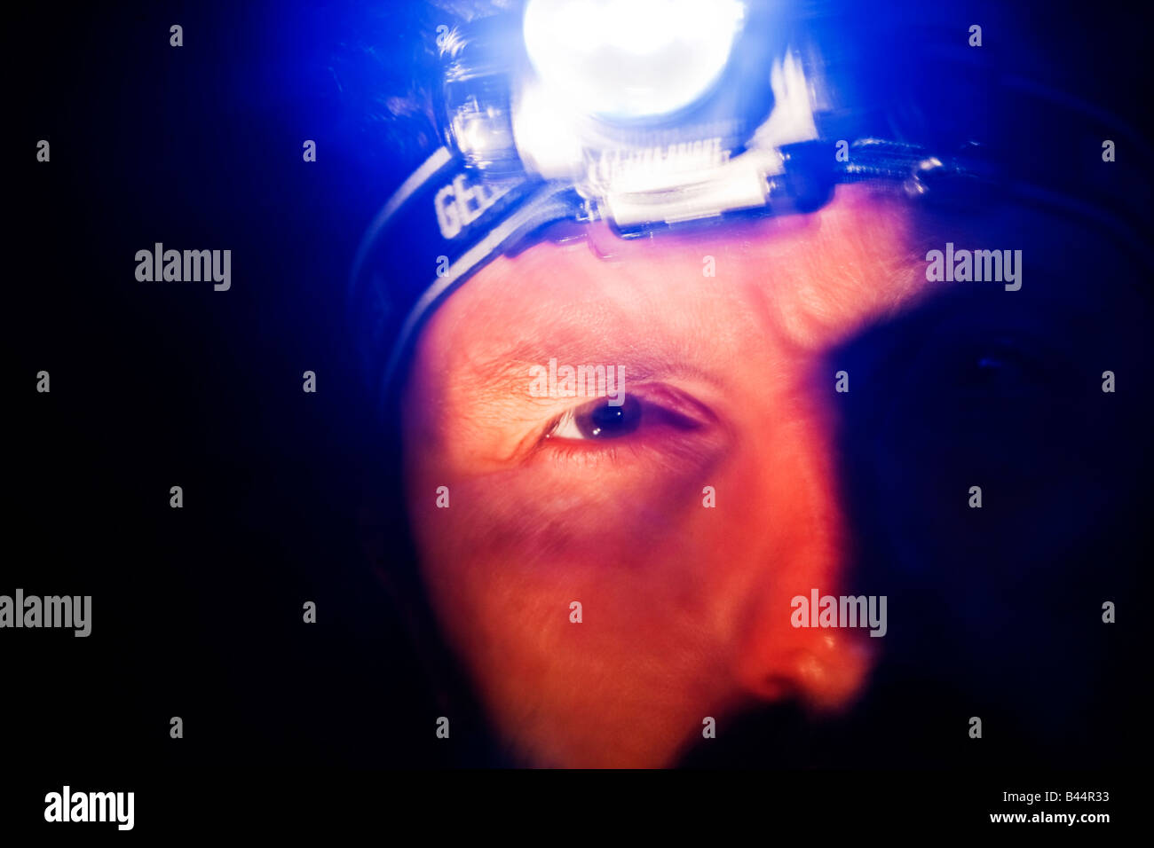 Male head wearing an LED headtorch in a darkened survival situation Stock Photo