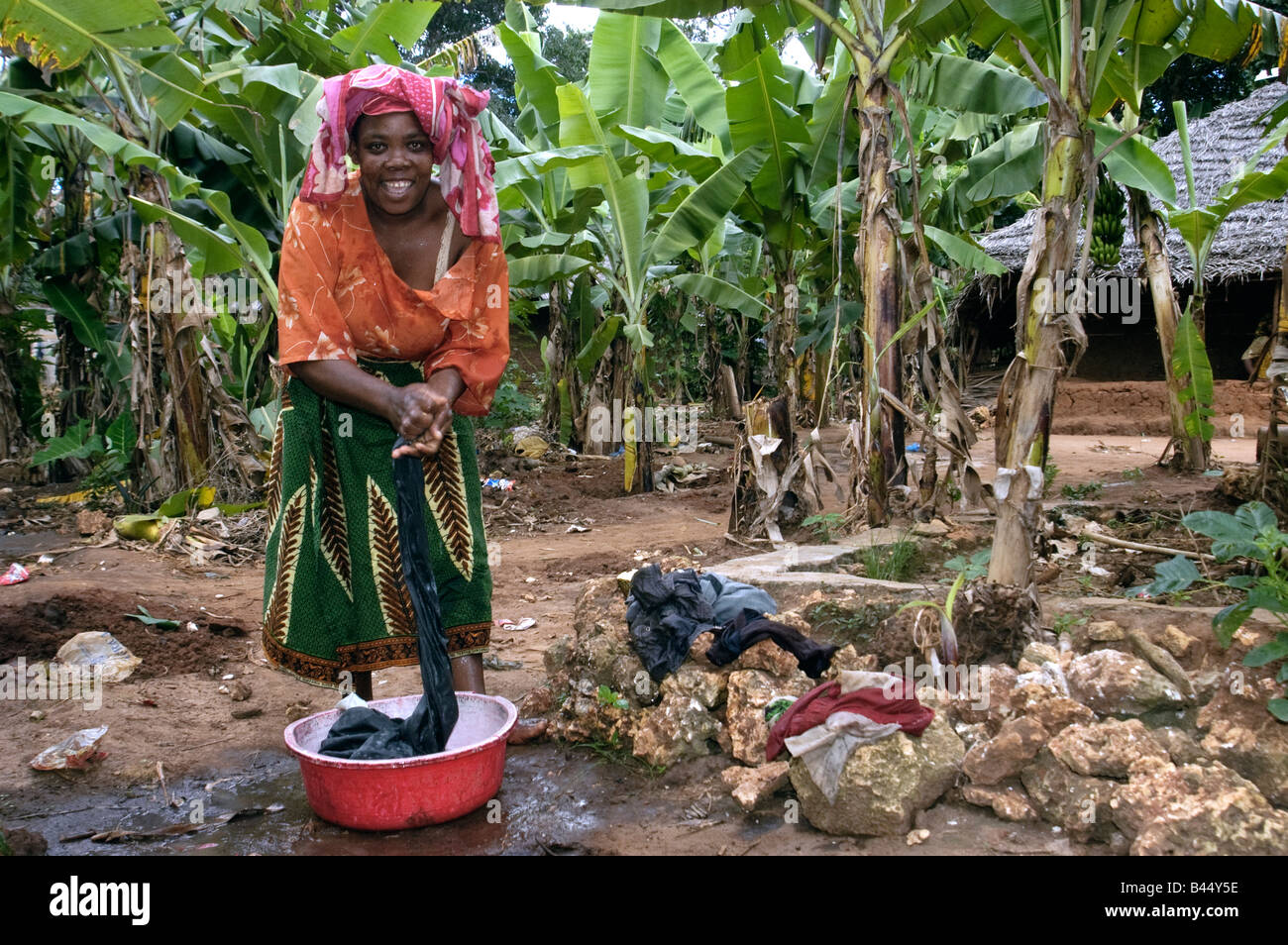 A woman washes clothes at a tap in her small banana plantation Zanzibar Tanzania Stock Photo