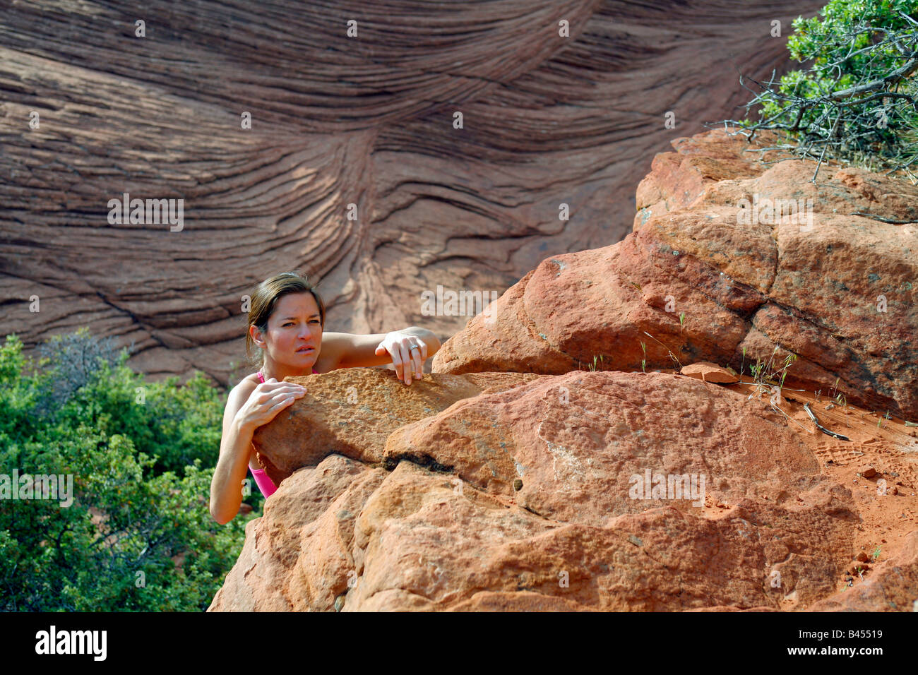 A woman lifts herself over the jagged edge of the cliffs at Snow Canyon ...
