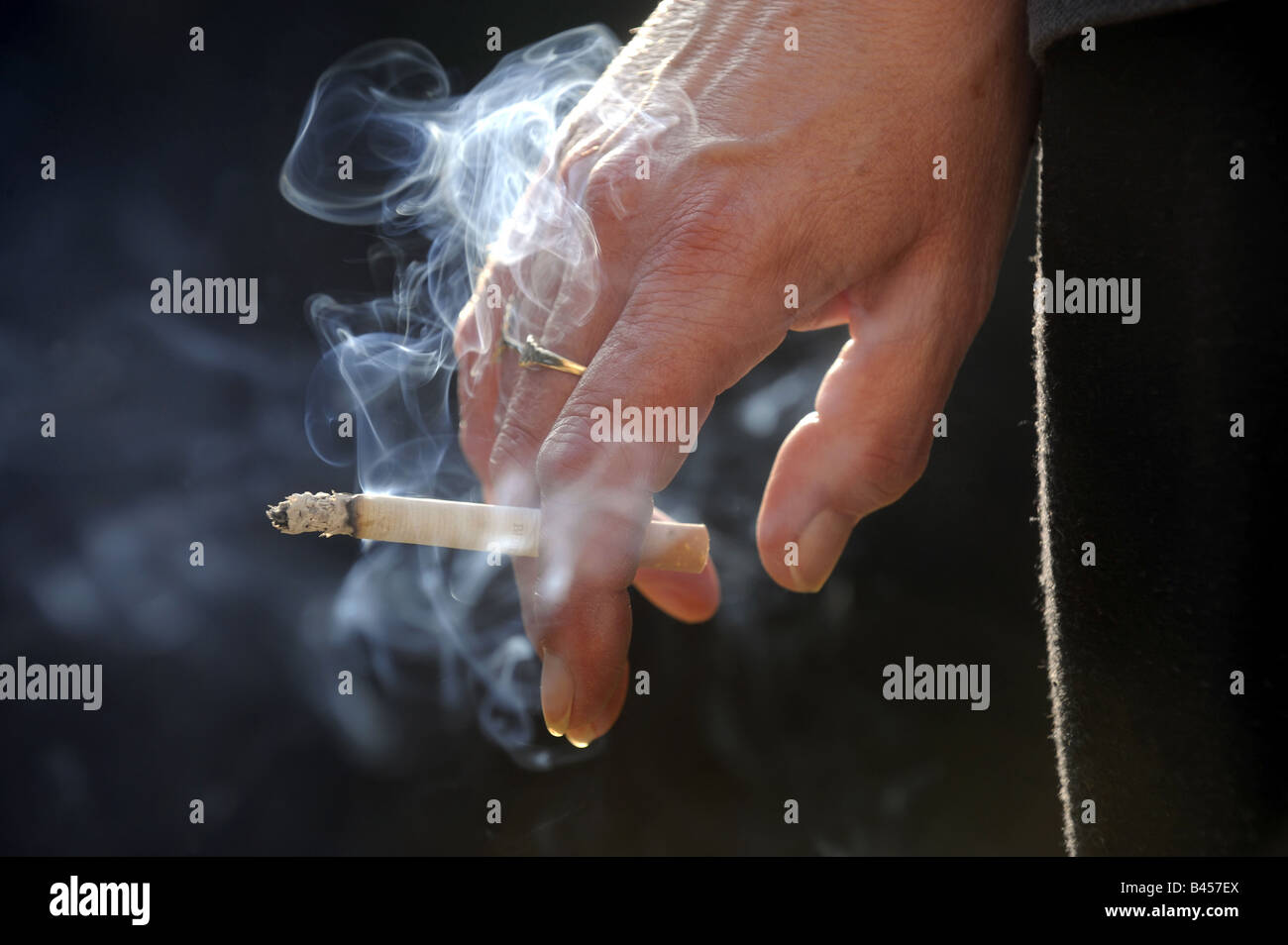 A  LIT CIGARETTE SMOKING IN A WOMANS HAND.RE HEALTH HEALTHY LIFESTYLE LUNG DISEASE LUNGS SMOKERS HOSPITALS UK CANCER Stock Photo