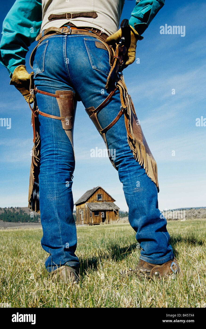 Backside of cowboy wearing jeans, pistol & chaps. Stock Photo