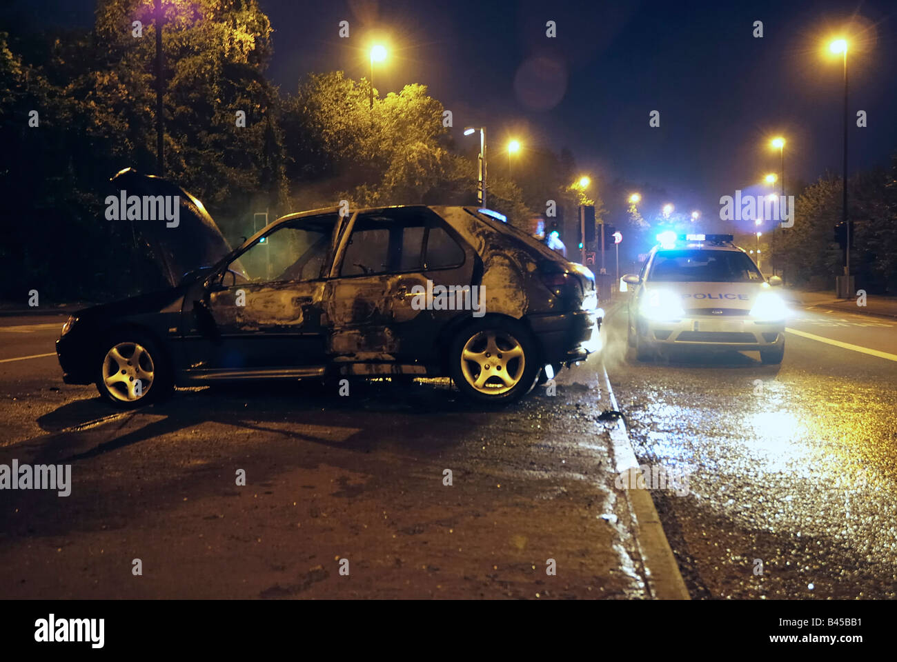 Burned out  car attended to by the police in the early hours of the morning Stock Photo