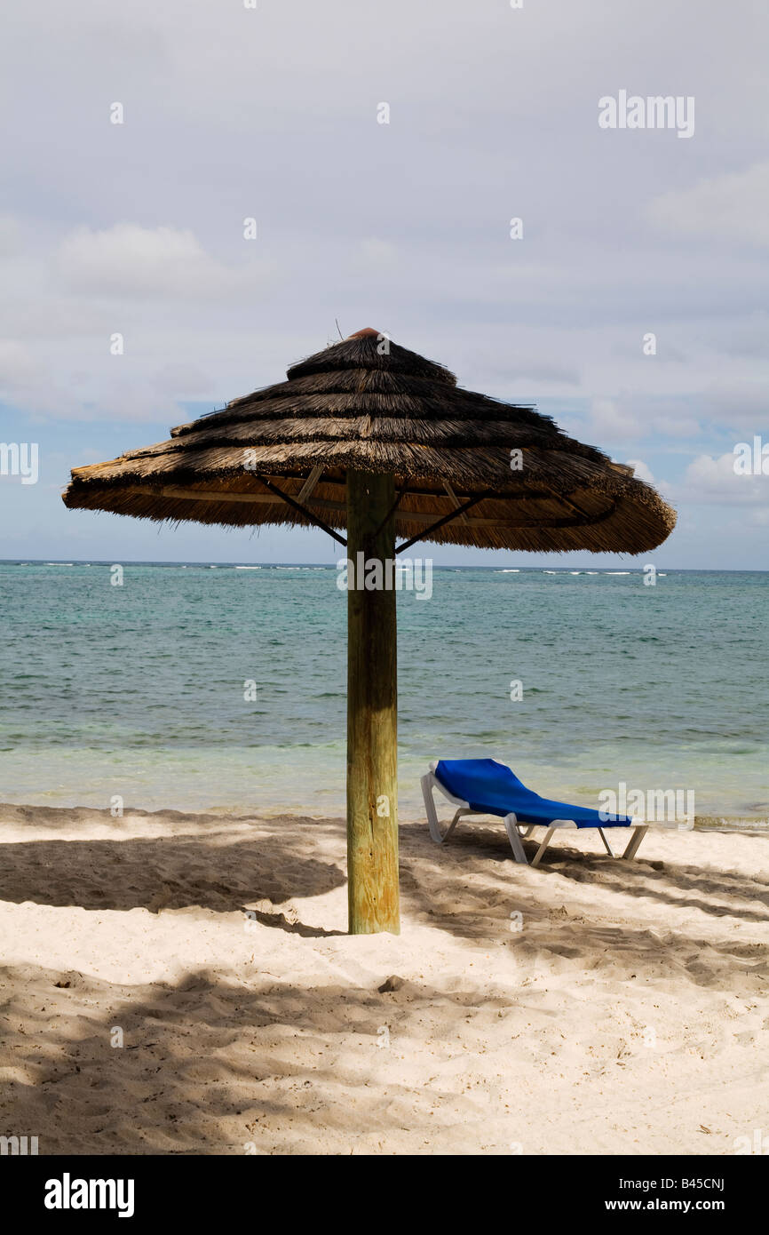 A blue sun bed and straw parasol for shade on a beach on the Carribean island of Antigua Stock Photo