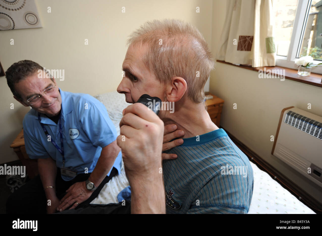A Homecare Assistant helps a brain damaged man to shave in his own home, Bradford. Stock Photo