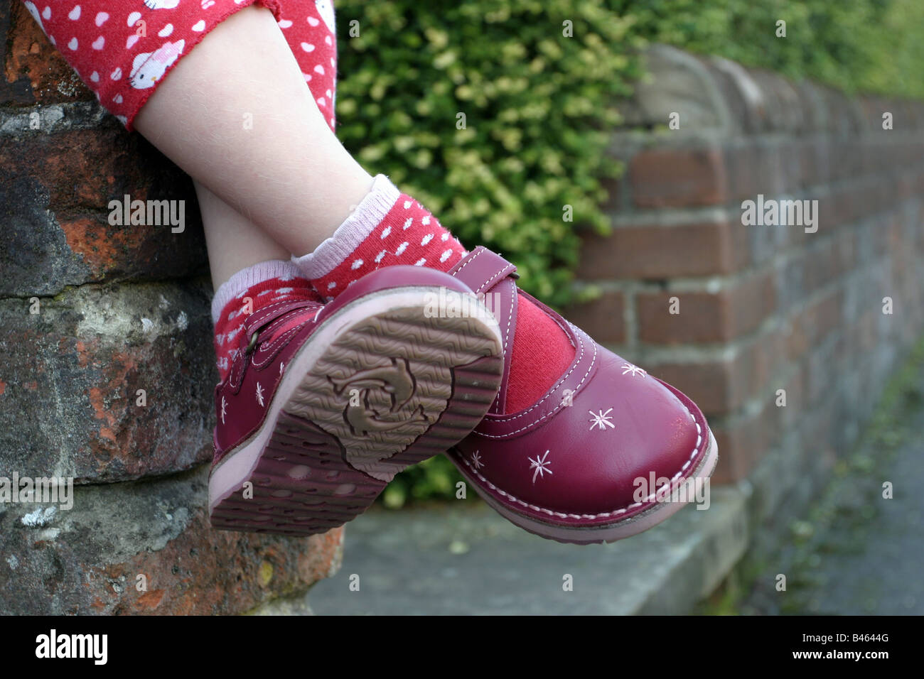 Young girl sitting on a garden wall, with her legs crossed,  wearing new red leather shoes Stock Photo