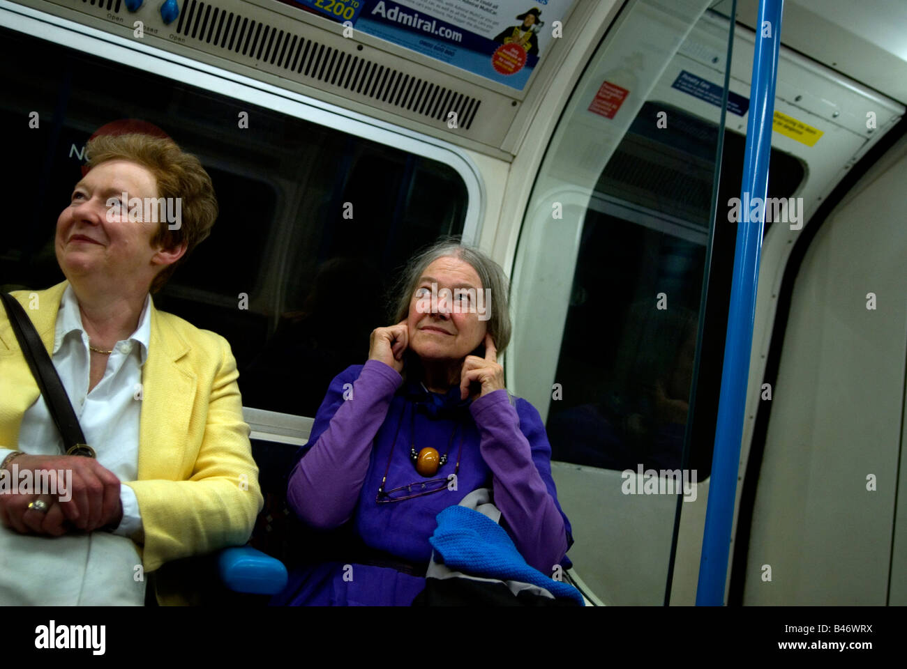 Two women on a tube train in London One is protecting her ears against the tube train noise Stock Photo