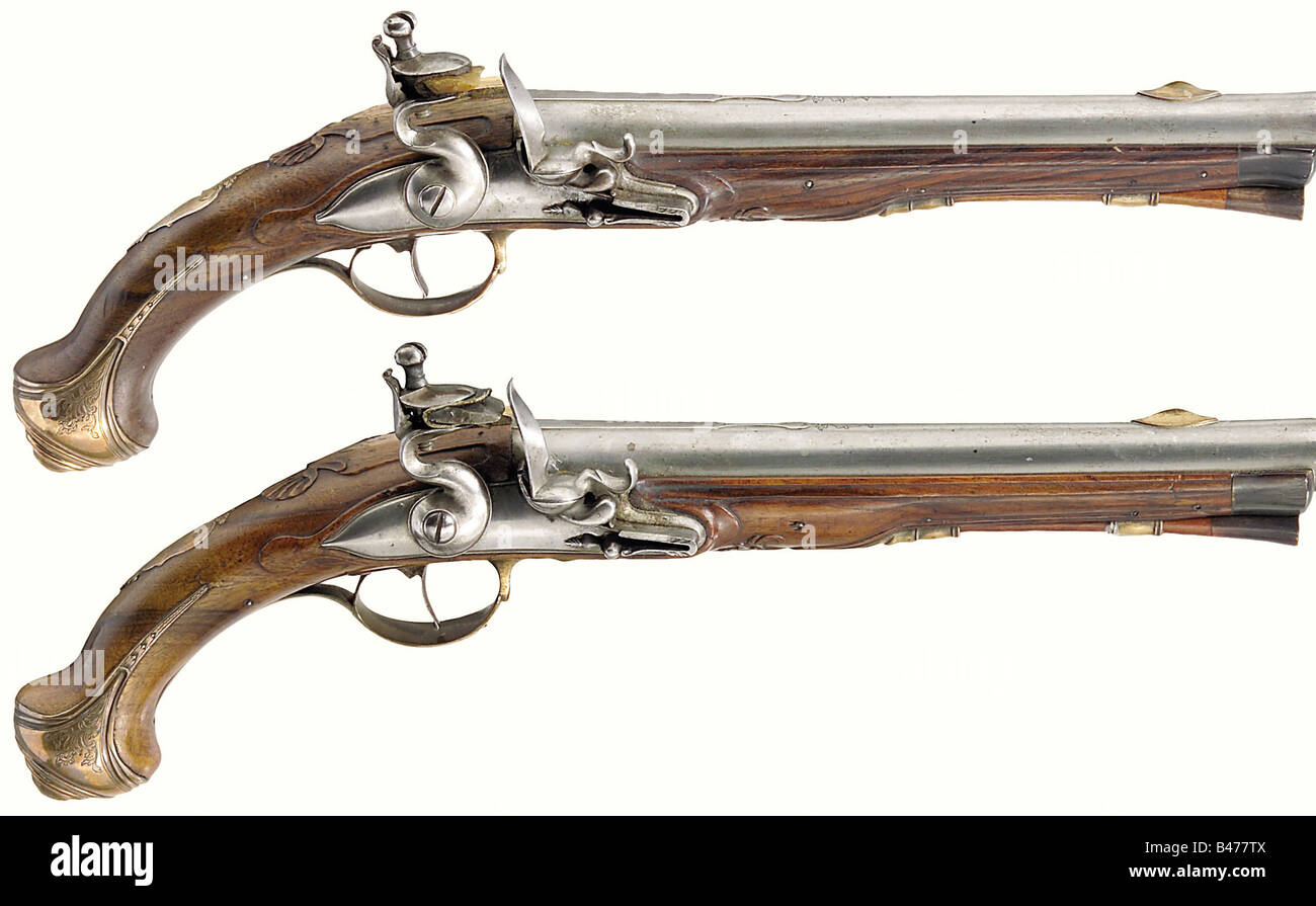 A pair of officer's flintlock pistols, middle of the 18th century. Round barrels, slightly swamped at the muzzles, at the breeches flats engraved with vine decoration, front and rear sights of bronze, smooth bores in 15 mm calibre. Iron banana flintlocks, the powder pans still have the original bluing in places. Walnut stocks carved with shell and plant decoration. Horn nose caps. Bronze furniture with engraved floral decoration. Lengths 34.5 cm. A good pair of pistols in very good condition. historic, historical, 18th century, civil handgun, civil handguns, ha, Stock Photo