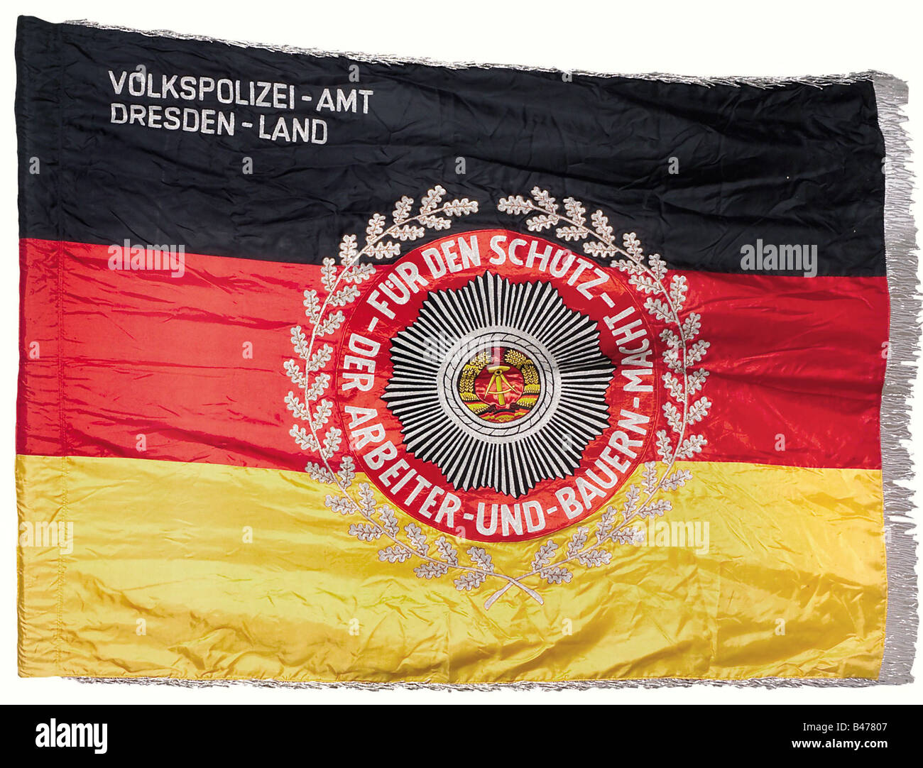 The GDR Volkspolizei., A banner for the Dresden regional office. Silk banner with silver fringe. Inscription on the upper left reads: 'Volkspolizei-Amt Dresden Land' (Volkspolizei Dresden Regional Office) and there is an embroidered national coat of arms on a star 'Für den Schutz der Arbeiter-und-Bauern-Macht' (For the Protection of the Workers and Peasants Power) and with an oak leaf wreath. Ca. 155 x 116 cm. historic, historical, 20th century, GDR, East Germany, Eastern Germany, East-German, East German, object, objects, stills, clipping, cut out, cut-out, cu, Stock Photo