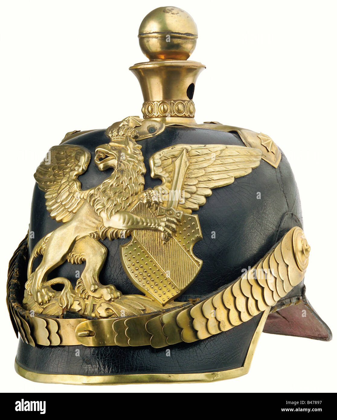 Baden: A helmet for officers, of artillery, as worn circa 1870. The crown of the leather skull is somewhat sunken, the left side is torn above the ear, and the lacquer finish is crazed. The large plate is of the older pattern. Flat chinscales are attached to a large officers' style cockade. The liner and the lining of the peak are of black leather, and show some signs of wear and ageing. Size 57. historic, historical, 19th century, object, objects, stills, clipping, clippings, cut out, cut-out, cut-outs, Stock Photo