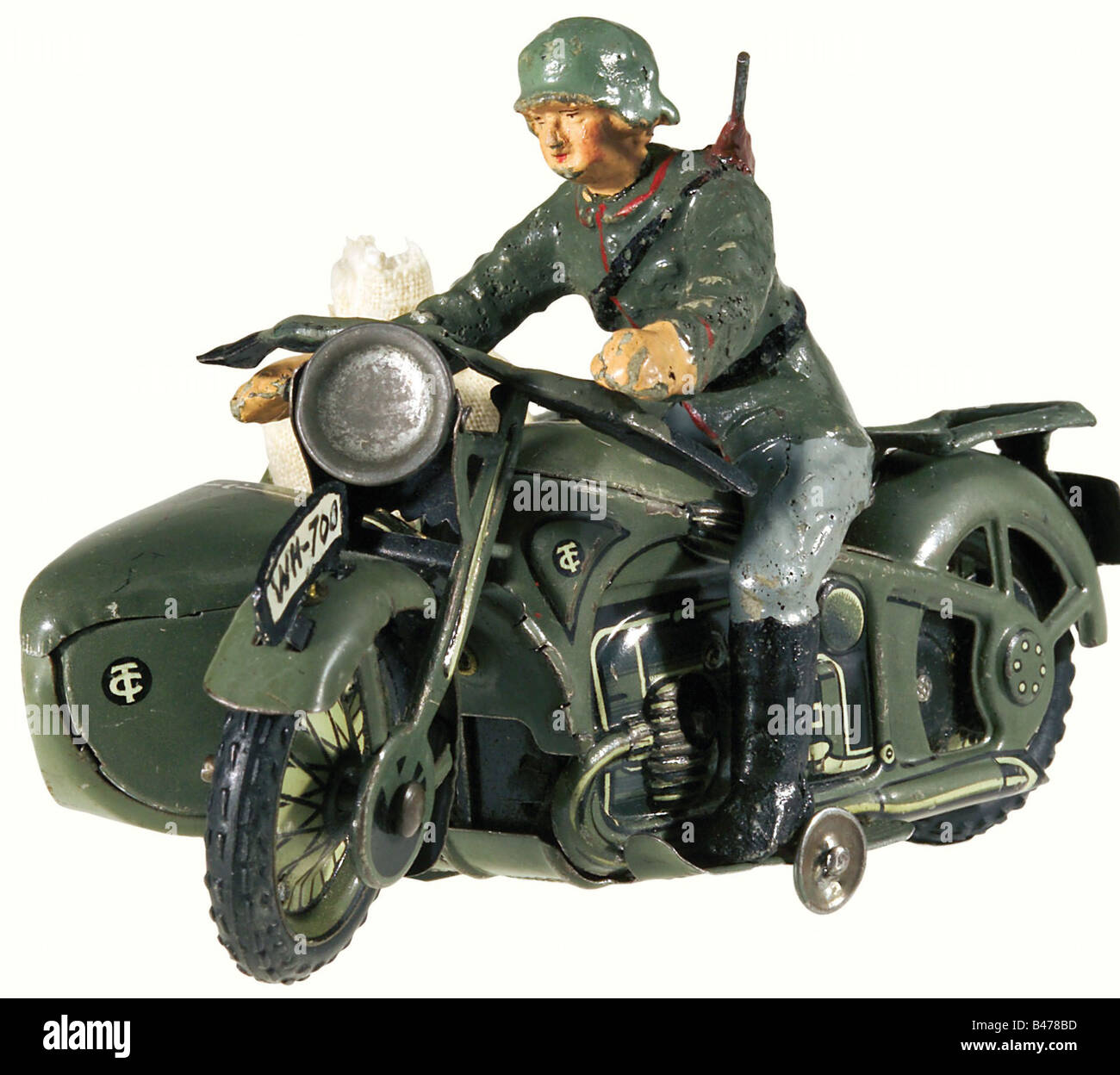 A motorcycle/sidecar combination, by the Tipp-Co. Company. Field grey lacquered/lithographed, full sheet metal version with rubber tires, moveable front wheel, functioning clockwork drive and parking brake. Motorcycle and sidecar have wire hook connectors. The motorcyclist (composition material) has a steel helmet and slung rifle. There is a mailbag in the sidecar. Dimensions: Length 14, Width 8, Height 5.5 cm. The number plates, the steering bar instruments, and the load carrier have been repainted in colour. Very rare sheet metal toy by the manufacturer Tipp-, Stock Photo